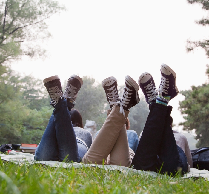 Photo des jambes de trois ado étendus sur une couverture dans l'herbe.
