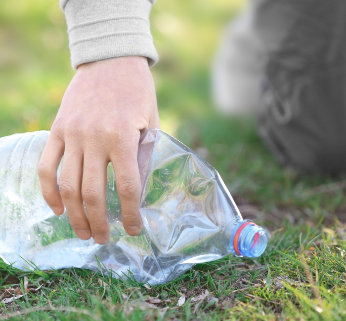 Main ramassant une vieille bouteille de plastique sur la pelouse.